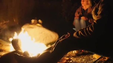 Genç bir adam ve bir kız şöminenin yanında katlanan sandalyelerde oturup konuşuyorlar..