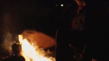 Genç bir adam ve bir kız şöminenin yanında katlanan sandalyelerde oturup konuşuyorlar..