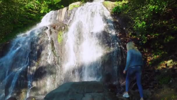 바위 위에서 있는 가느다란 금발의 어린 소녀가 열 대의 폭포를 연상한다 — 비디오