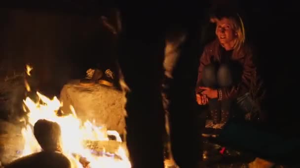Giovane ragazzo e una ragazza sono seduti su sedie pieghevoli vicino al fuoco e parlando. — Video Stock