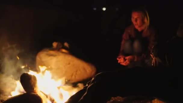 Jeune homme et une fille sont assis sur des chaises pliantes au coin du feu et parlent. — Video