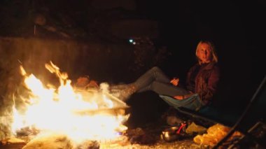 Genç bir adam ve bir kız şöminenin yanında katlanan sandalyelerde oturup konuşuyorlar..