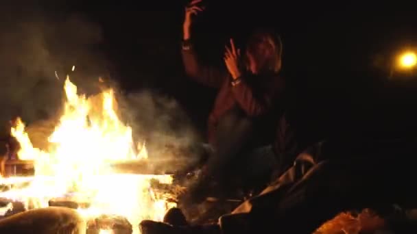 젊은 남성 과 소녀는 불옆에 접는 의자에 앉아 이야기하고 있습니다.. — 비디오