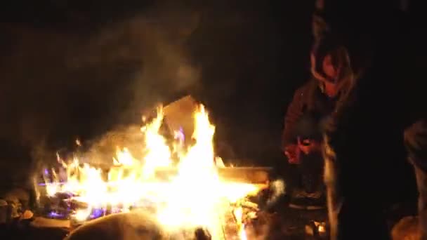 Chico joven y una chica están sentados en sillas plegables junto al fuego y hablando. — Vídeo de stock