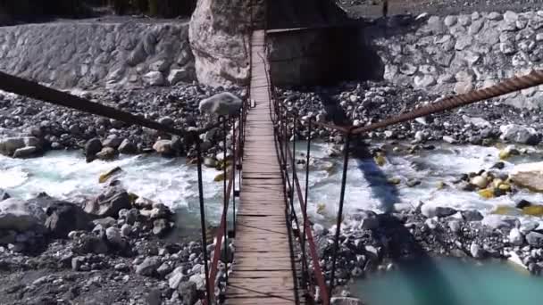 Un vecchio ponte sospeso pedonale passa attraverso un fiume tempestoso di montagna. — Video Stock