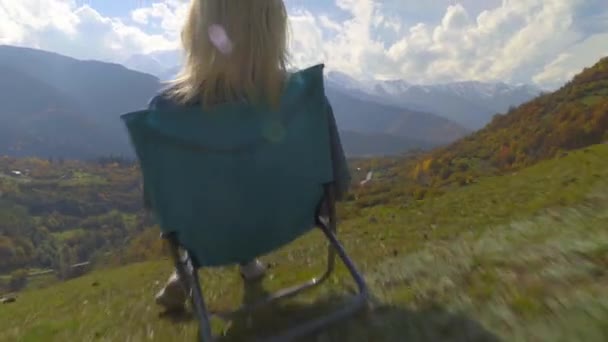 Una mujer se sienta en una silla y observa el valle de la montaña en otoño. — Vídeos de Stock