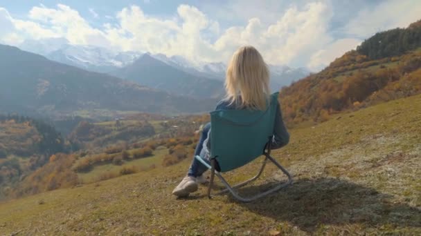 Жінка сидить на стільці і спостерігає за гірською долиною восени . — стокове відео