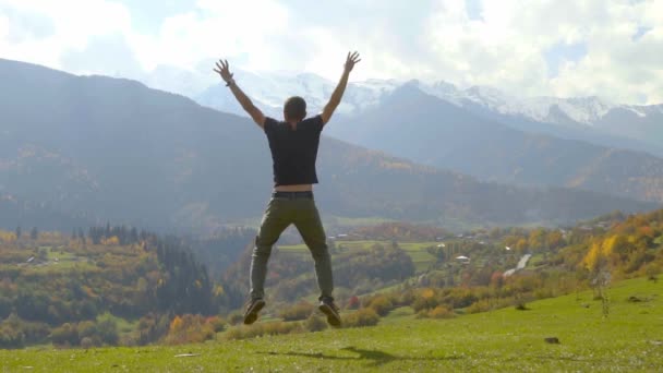 Чоловік стрибає і плескає руками на тлі осінніх гір . — стокове відео
