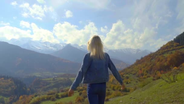Жінка в джинсовій куртці стоїть на вершині гори, піднімаючи руки в повітрі , — стокове відео