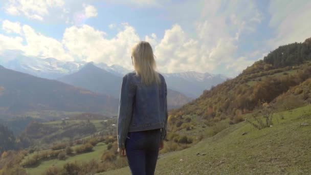 Женщина в джинсовой куртке стоит на вершине горы, поднимая руки в воздух, — стоковое видео