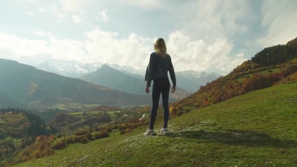 Femme en jean veste est debout sur le sommet de la montagne, levant les mains dans l'air, — Video