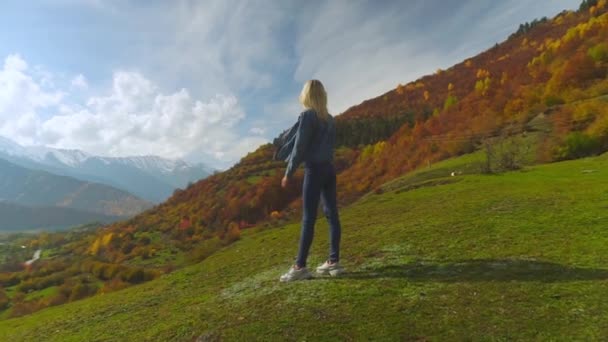 Femme en jean veste est debout sur le sommet de la montagne, levant les mains dans l'air, — Video