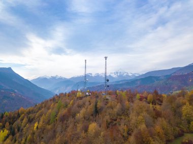 Bir sonbahar günü dağlardaki ormanda antenli iki yüksek voltajlı kulenin insansız hava aracı görüntüsü..