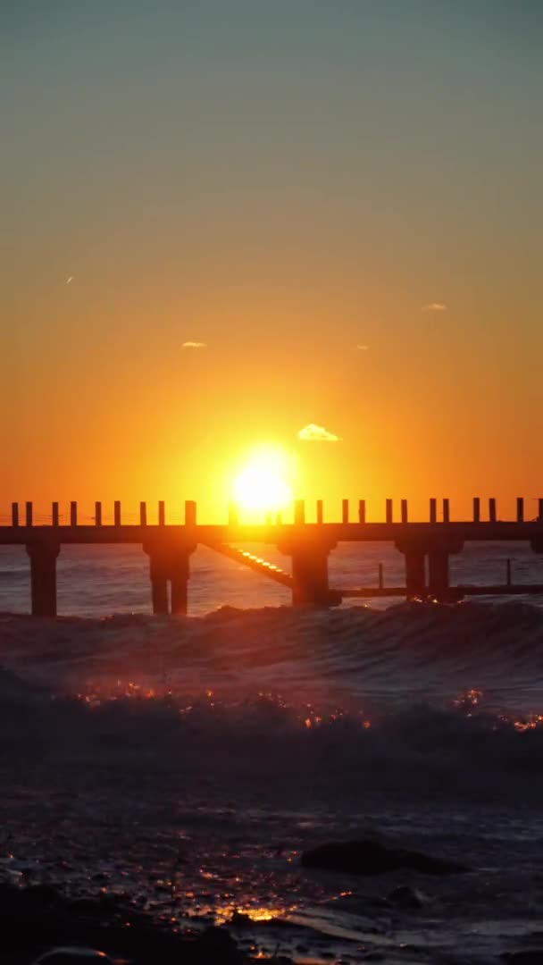 Varma stormvågor träffade piren vid solnedgången. Vacker orange himmel, kraschar vågor. — Stockvideo