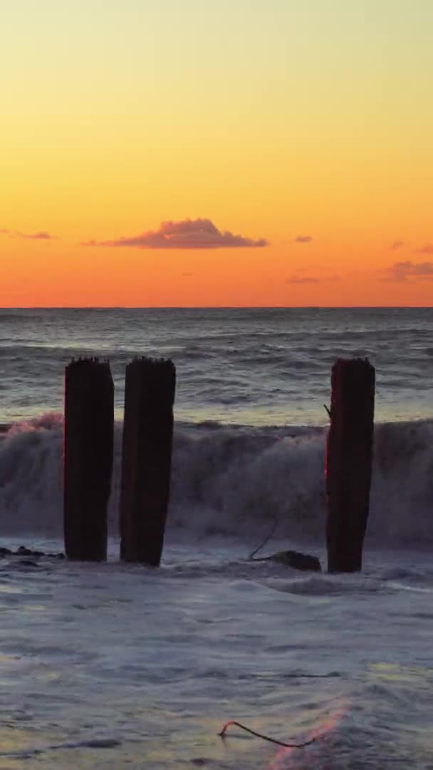 Vågor kraschar mot gamla armerade betongpelare på stranden vid solnedgången — Stockvideo