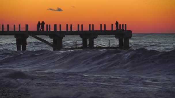 Zonsondergang op de achtergrond van de pier waar silhouetten van mensen lopen. — Stockvideo