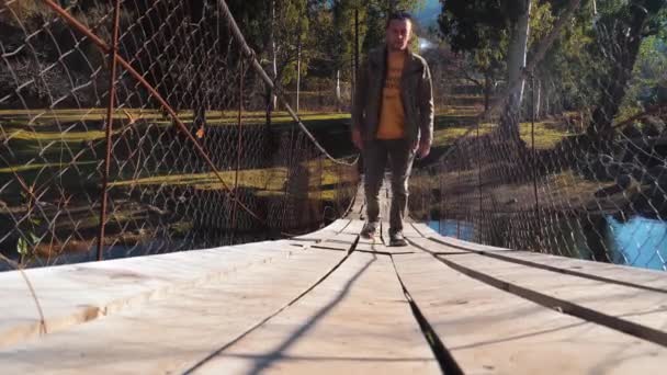 Un joven turista camina sobre un puente colgante de madera, — Vídeos de Stock