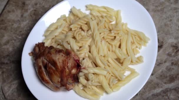 A white plate with boiled pasta and fried chicken leg rotates around its axis — Video Stock