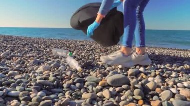 Plajda plastik şişe toplayan bir kadın.,