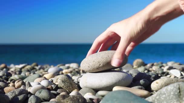 Το χέρι μιας γυναίκας φτιάχνει μια πυραμίδα από πέτρες στο φόντο της θάλασσας ή του ωκεανού.. — Αρχείο Βίντεο