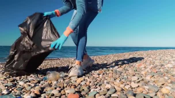 Жінка збирає чистячі пластикові пляшки на пляжі , — стокове відео