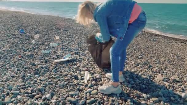 검은 쓰레기통에 쓰레기를 모으는 한 여성 자원 봉사자. — 비디오