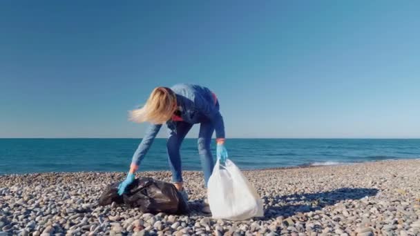 A female volunteer collects garbage in a black garbage bag. — Stockvideo