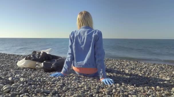 Žena v džínovém obleku sedí na pobřeží po sbírání odpadků, — Stock video