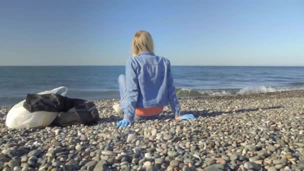 Kobieta w dżinsowym garniturze siedzi na brzegu po zbiórce śmieci, — Wideo stockowe
