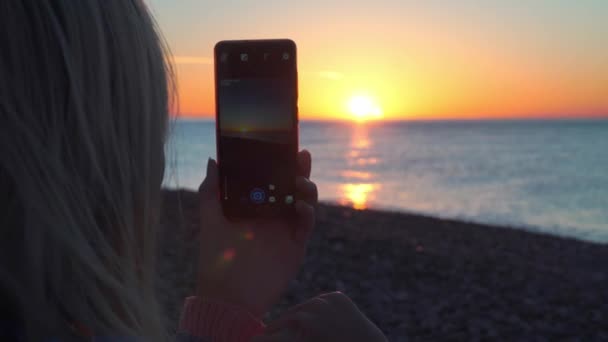 Kvinnors händer hålla en smartphone och ta bilder av solnedgången på havet. — Stockvideo