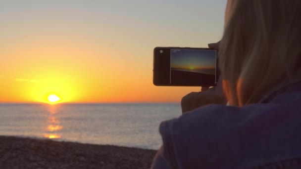 Le mani delle donne tengono uno smartphone e fotografano il tramonto sul mare. — Video Stock