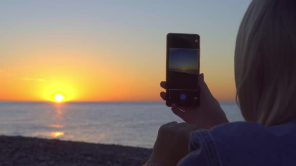 Kvinnors händer hålla en smartphone och ta bilder av solnedgången på havet. — Stockvideo