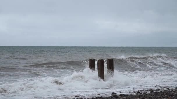 Fale burzowe zderzają się ze starymi słupami żelbetowymi na plaży — Wideo stockowe