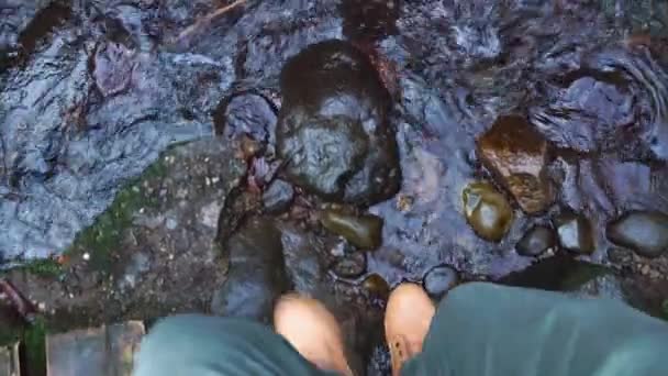 Close-up of legs of male traveler walking along stones on mountain river. — Stock Video