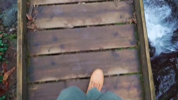 Close-up of legs of male traveler walking across a bridge to mountain river. — стоковое видео