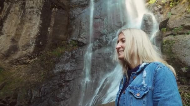 A young traveler smiled at the camera and enjoyed the wildlife with a waterfall — Stockvideo