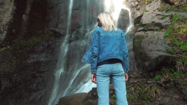 The girl is facing the waterfall and with her back to the camera. — Stock Video