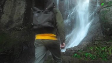 Sırt çantalı bir adam ormanın derinliklerindeki şelaleye tek başına yürüyor..