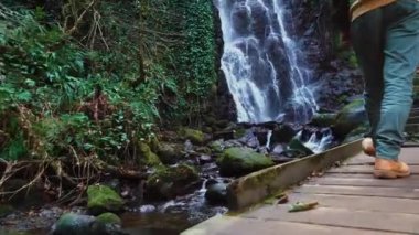 Adam Gürcistan 'daki Mirveti şelalesinin arka planında tahta köprüde yürüyor..