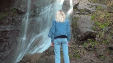 Kız şelaleye bakıyor ve sırtı kameraya dönük..