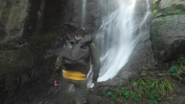 Homme avec sac à dos sur le dos marche seul à la chute d'eau dans la jungle des profondeurs. — Video