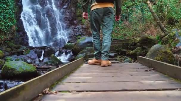 Man loopt op houten brug tegen achtergrond van Mirveti waterval in Georgië. — Stockvideo