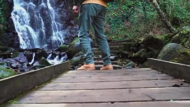 Człowiek chodzi po drewnianym moście na tle wodospadu Mirveti w Gruzji. — Wideo stockowe