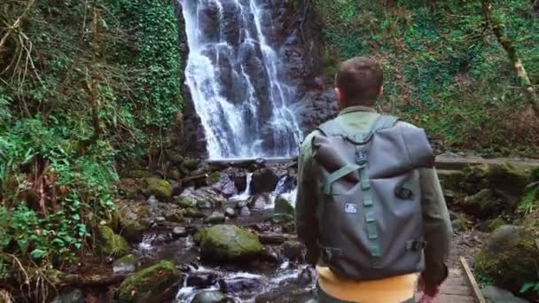 Man loopt op houten brug tegen achtergrond van Mirveti waterval in Georgië. — Stockvideo