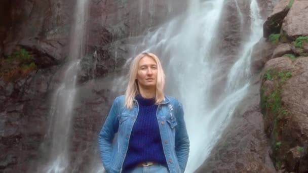Mujer sostiene el teléfono inteligente y toma fotos de sí misma de pie cerca de la cascada — Vídeo de stock