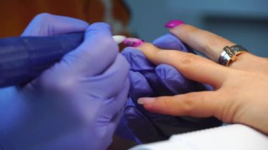 Manicure master in blue gloves removes gel polish from nails using a cutter.
