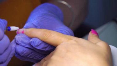 Manicure master in blue gloves removes gel polish from nails using a cutter.