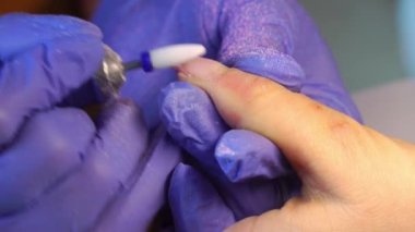 Manicure master in blue gloves removes gel polish from nails using a cutter.