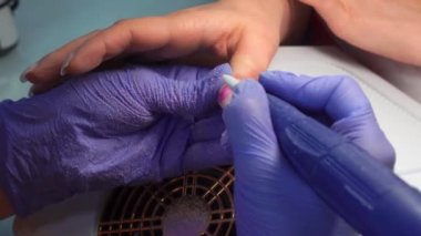 Manicure master in blue gloves removes gel polish from nails using a cutter.