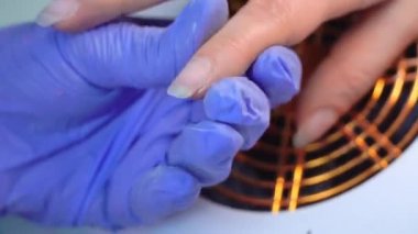 Close-up of manicure master in blue gloves filing nails with special nail file.